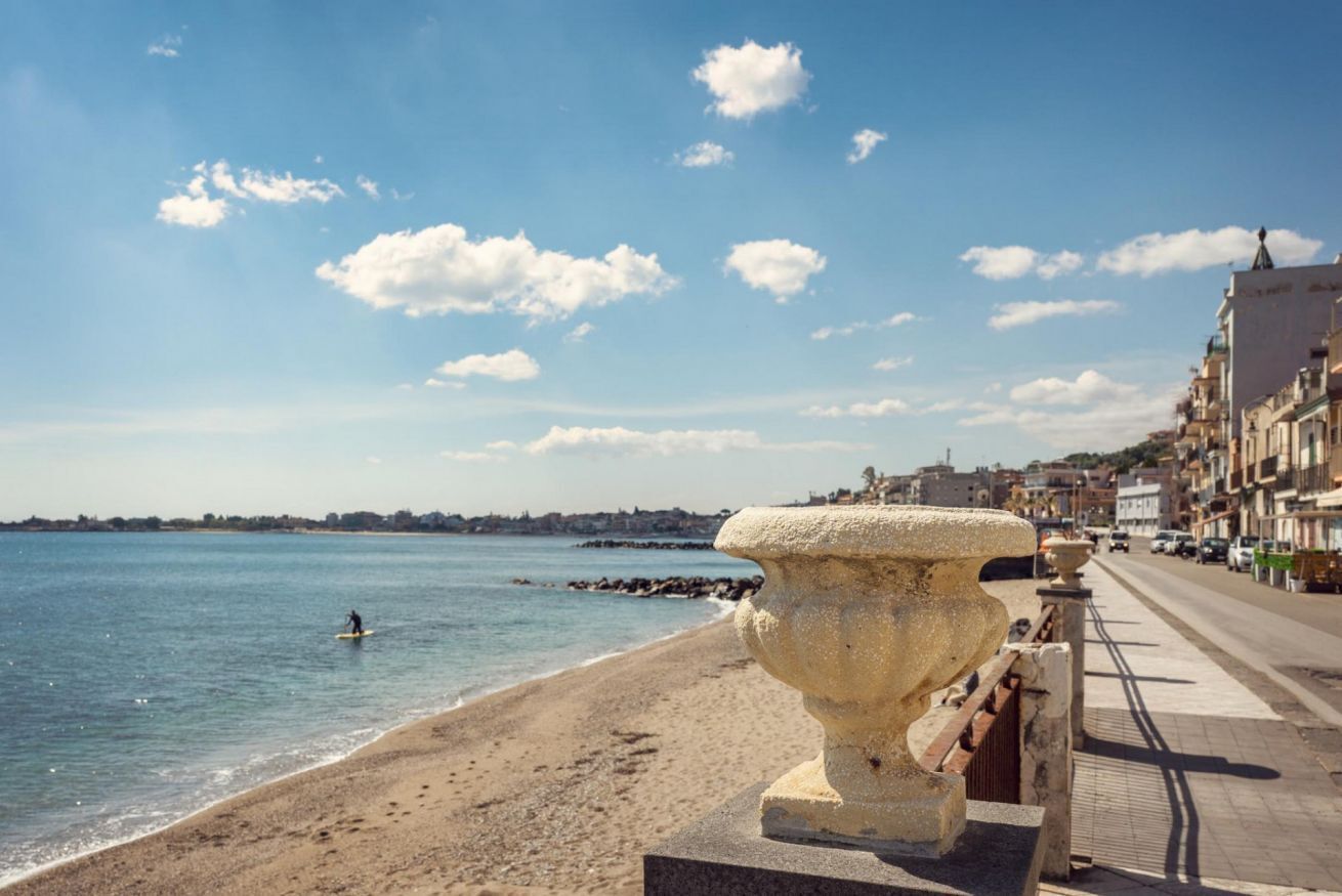 A beach with a stone balustrade, a clear sky, and a calm sea.