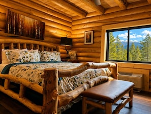 A log cabin bedroom with a bed, bench, and a window with a mountain view.