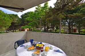 A balcony with a table set for breakfast, including bread, pastries, fruit, and beverages. - Two-level Flat for Groups in Lignano (Lignano Sabbiadoro)
