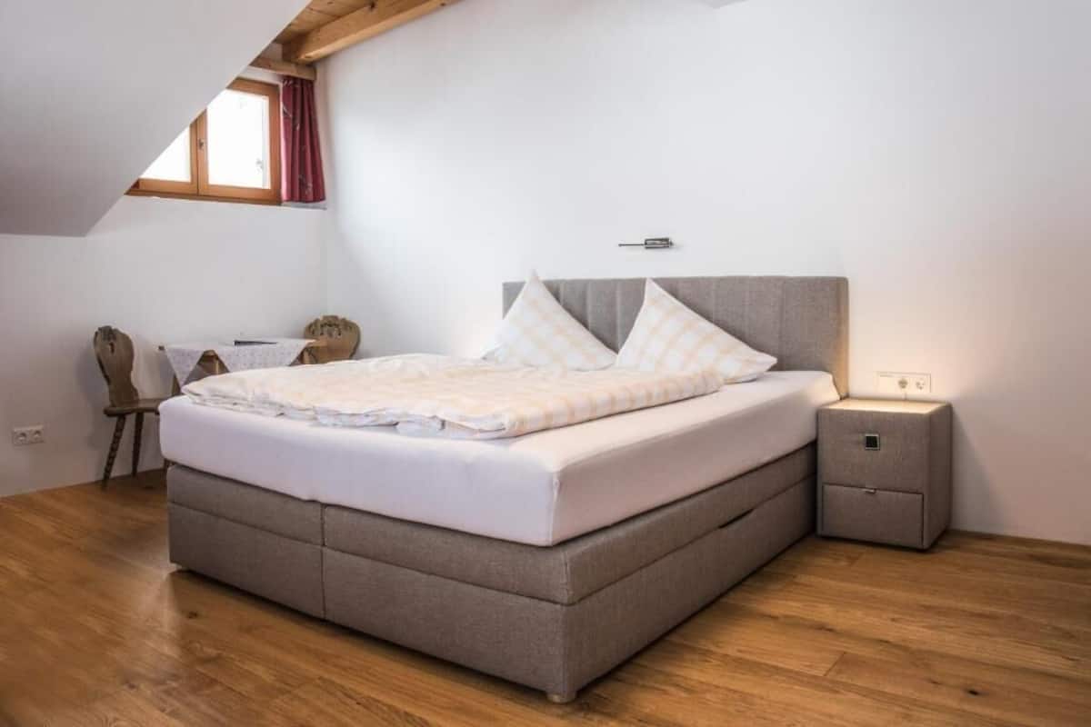 A bedroom with a bed, a nightstand, a desk, and a window.