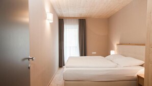 Ein Schlafzimmer mit einem Bett, einem Nachttisch, einer Wandleuchte und einem Fenster mit Vorhängen.