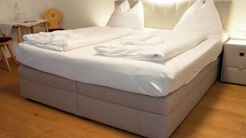 A neatly made bed with pillows and folded towels, a bedside table with a lamp, and a wooden chair.
