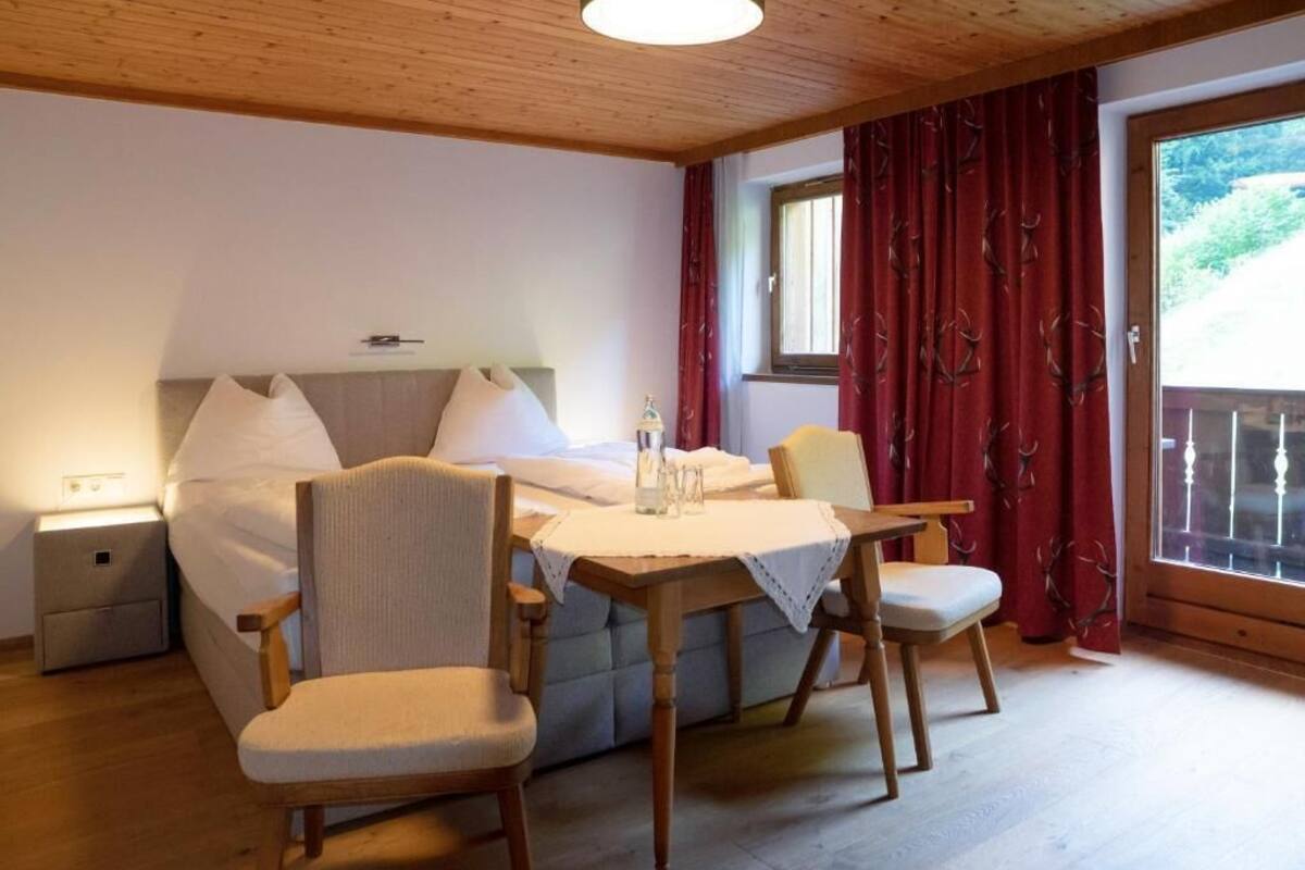 A room with a bed, a table with chairs, a nightstand, and a window with curtains.