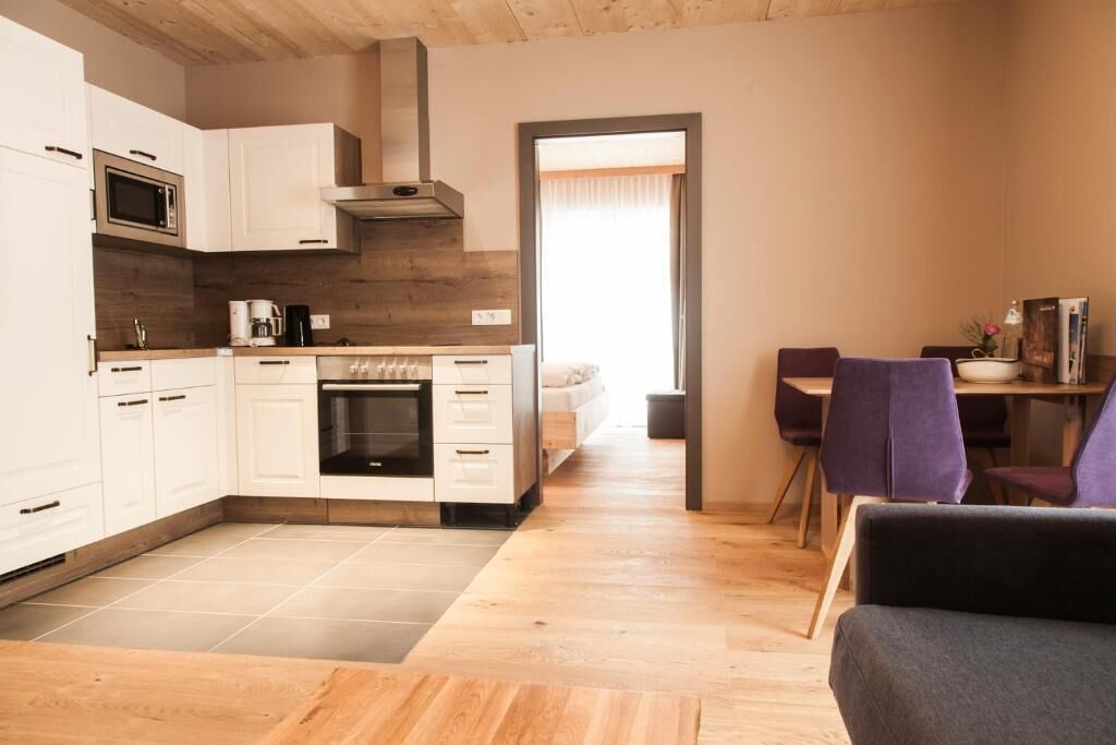 A modern kitchen with white cabinets, a microwave, and a stove. There is a dining area with purple chairs and a table.