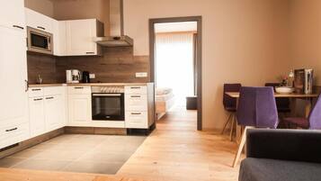 A modern kitchen with white cabinets, a microwave, and a stove. There is a dining area with purple chairs and a table.