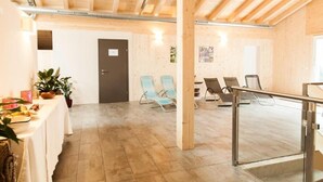 Ein geräumiger Raum mit hoher Decke, Holzbalken, einem Tisch mit Gegenständen und mehreren Stühlen.