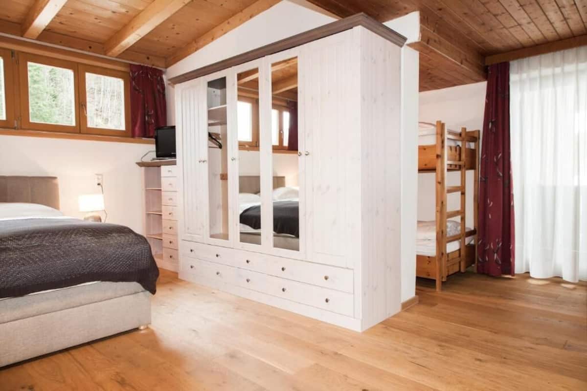 A bedroom with a bed, a wardrobe, a desk with a computer, and a bunk bed.