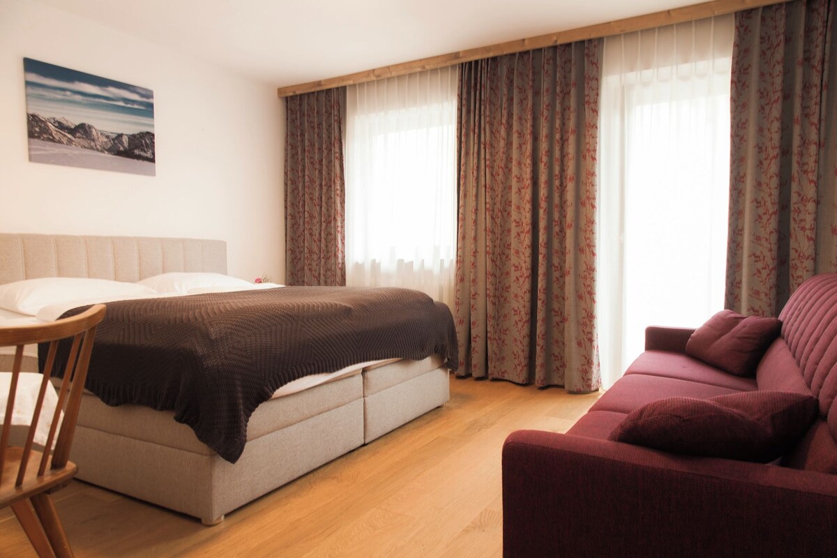 Un dormitorio con cama, sofá, sillón y un cuadro en la pared.