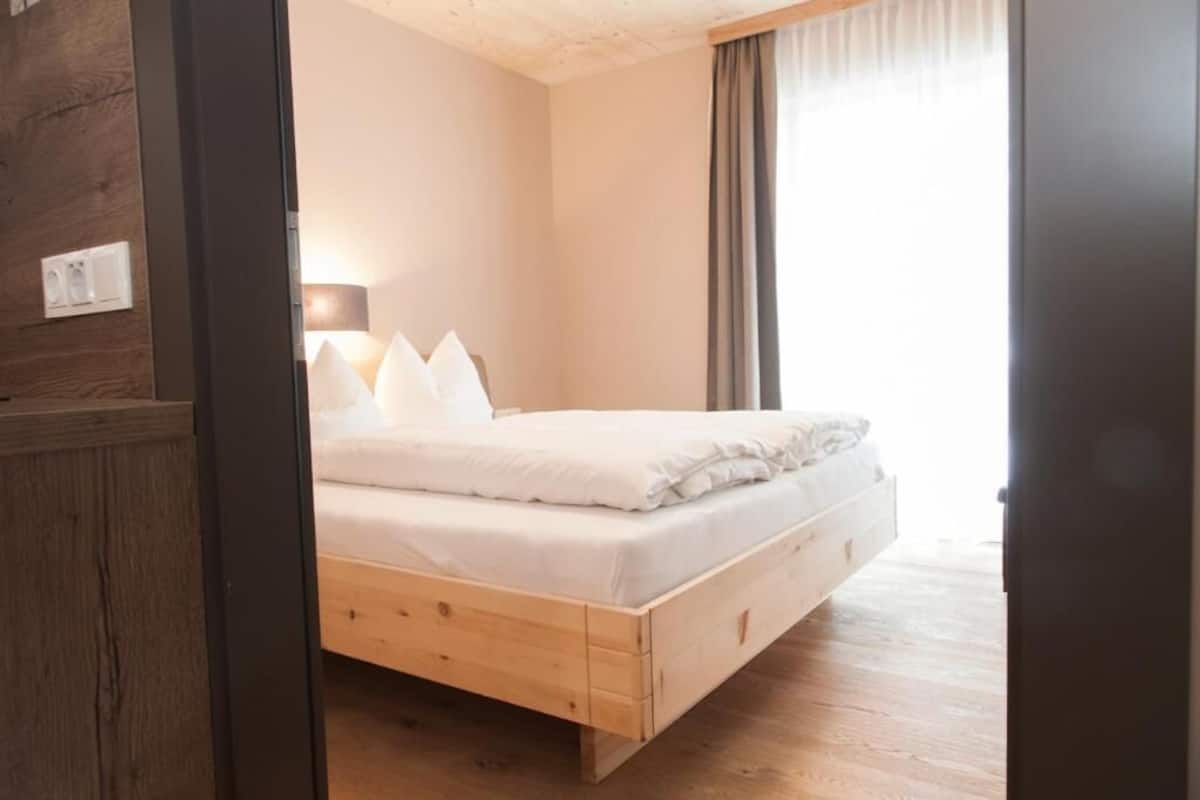 A bedroom with a wooden bed, a bedside lamp, and a window with curtains.