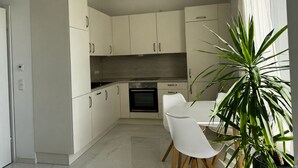 Eine moderne Küche mit weißen Schränken, einem eingebauten Backofen und einem Esstisch mit Stühlen.