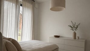 Ein Schlafzimmer mit Bett, Nachttisch, einer Pflanze in einer Vase und einer Hängeleuchte.