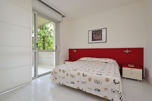 A bedroom with a bed, a nightstand, a red headboard, a window, and a framed picture on the wall. - Adorable Apartment With Pool (Lignano Sabbiadoro)