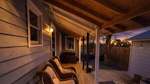 A covered porch with wooden flooring, a seating area with wicker chairs, and a view of a backyard. - Walk to Town & River • Fire Pit • King Bed (Kerrville)