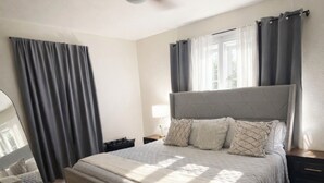 A bedroom with a bed, a ceiling fan, a nightstand, a lamp, and a window with curtains. - Walk to Town & River • Fire Pit • King Bed (Kerrville)