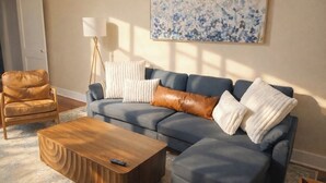 A living room with a sofa, a coffee table, a chair, and a floor lamp. - Walk to Town & River • Fire Pit • King Bed (Kerrville)