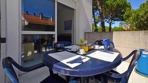 Une table à manger avec des chaises, une porte vitrée donnant sur un balcon et une poubelle bleue.