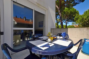 A dining table with chairs, a glass door leading to a balcony, and a blue trash bin. - Welcoming Apartment for Groups (Lignano Sabbiadoro)