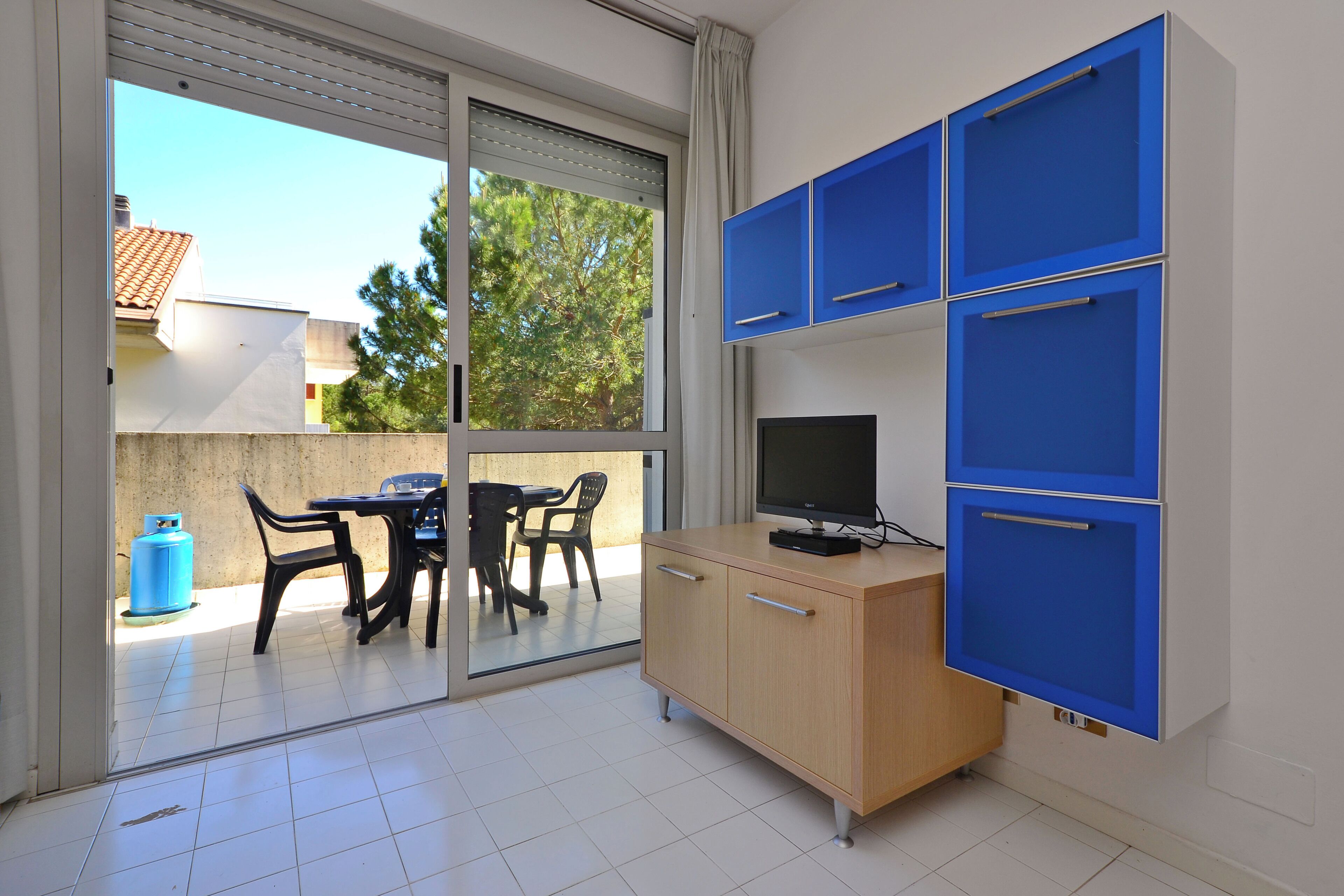 A room with a sliding glass door leading to an outdoor area, a wooden desk with a computer, and blue cabinets.