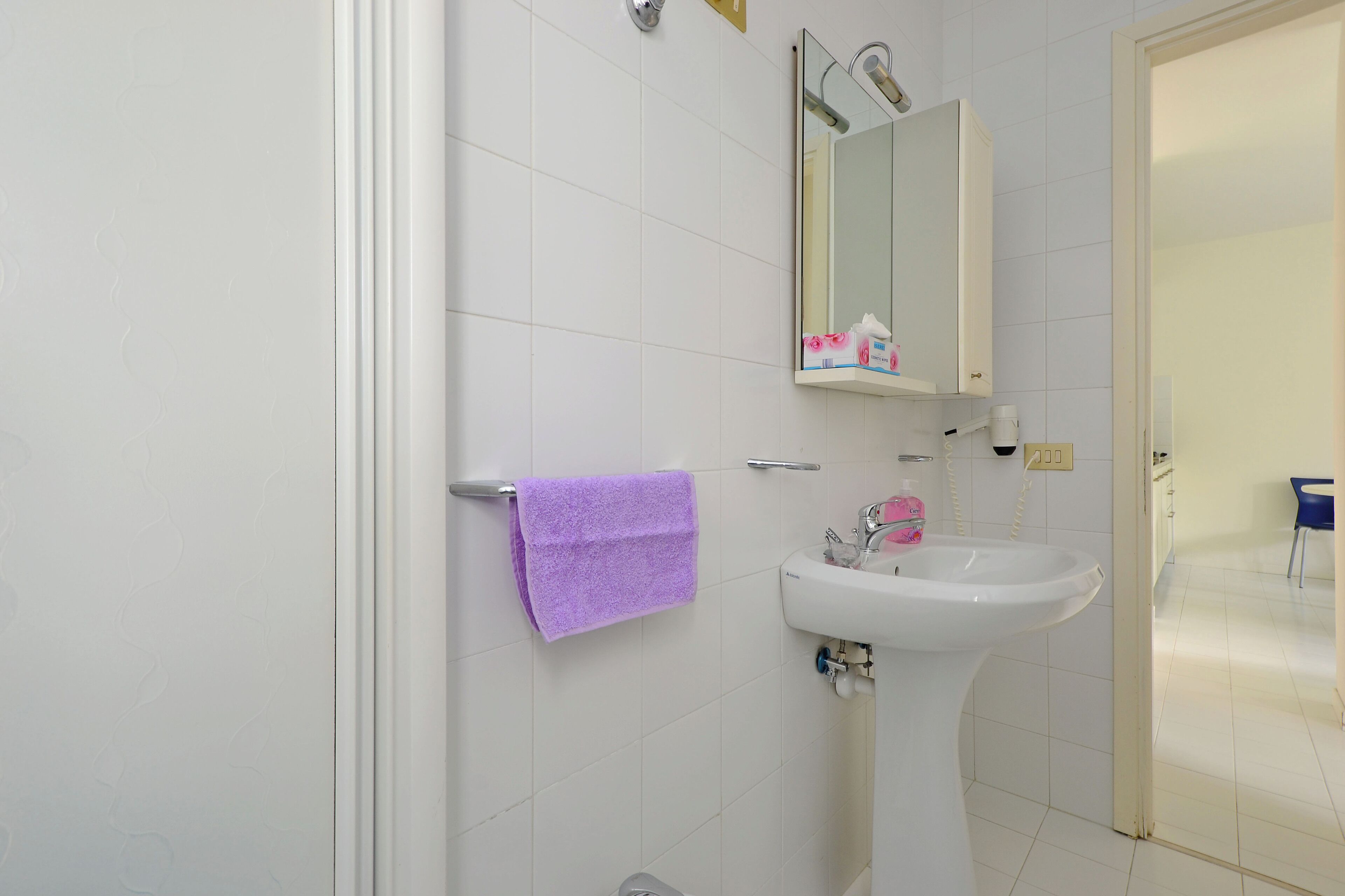 A bathroom with a white sink, a mirror, and a purple towel hanging on the wall.