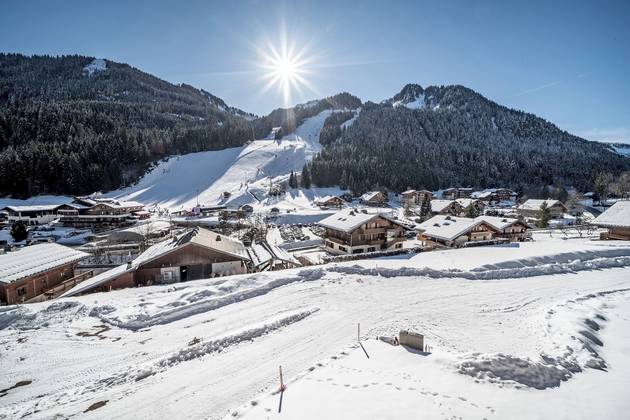 A snow-covered village with buildings, a ski slope, and a mountain backdrop.