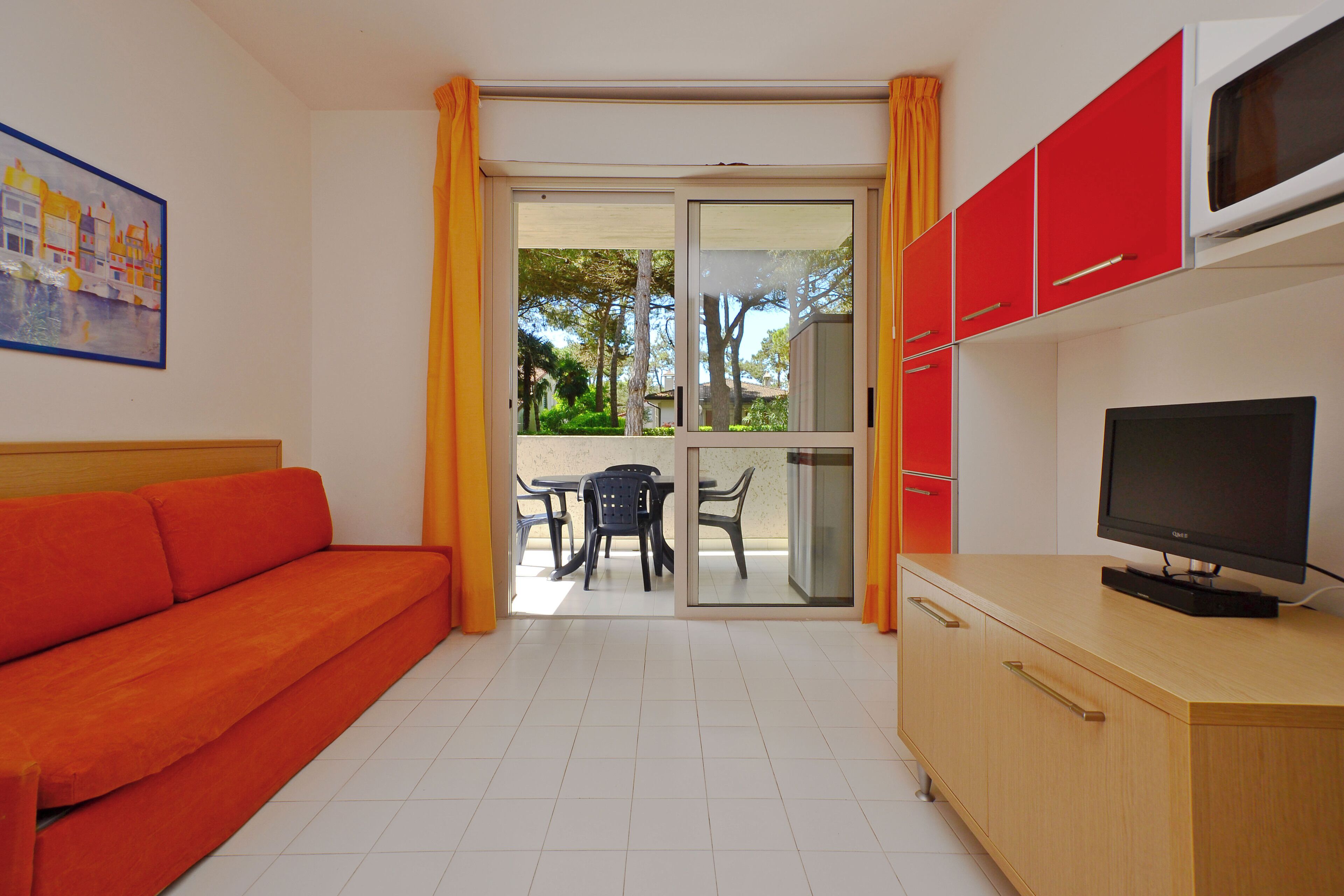 Una habitación con sofá, televisor sobre un mueble bajo y puerta corrediza de vidrio que da a un espacio exterior con mesa y sillas.