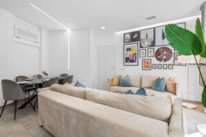 A modern living room with a beige sofa, dining table, and chairs. There are framed pictures on the wall and a large green plant. - Penthouse "Vivi Milano" in Duomo District + Comfort (Milano)