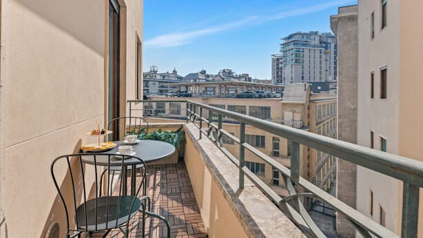 A balcony with a table and chairs, a small plant, and a view of city buildings. - Penthouse "Vivi Milano" in Duomo District + Comfort (Milano)