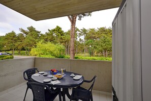 An outdoor dining area with a table set for four, surrounded by chairs, and a view of a park with trees and a road in the background. - Dreamy Apartment in a Quiet Area (Lignano Sabbiadoro)