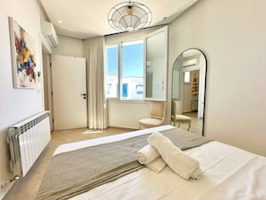 Quarto de hotel moderno com uma cama grande, um espelho, um radiador e uma janela com cortinas.