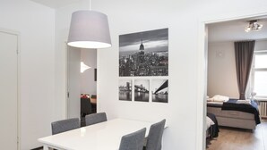 A modern room with a white table, grey chairs, a cityscape artwork, and a bed with a grey headboard. - Premium 4-Bedroom Stay in Central Helsinki (Helsinki)