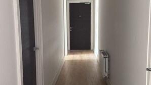 En gang med trægulv, en sort dør i enden og en radiator på højre væg.