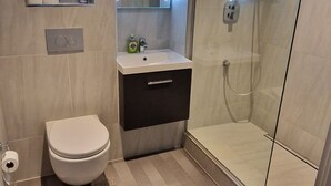 Et badeværelse med toilet, håndvask og brusekabine med glasvægge.