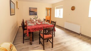 Ein Esszimmer mit einem Tisch für vier Personen, Holzsesseln, einer roten Tischdecke, einem Gemälde an der Wand und einem Fenster mit Jalousien.