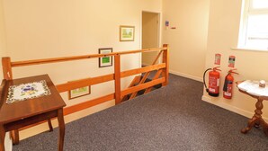 Ein Korridor mit einer Holzwandleiste, gerahmten Bildern an der Wand, einem kleinen Tisch mit einer Spitzenleinentischdecke und zwei an der Wand befestigten Feuerlöschern.