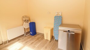 Ein Zimmer mit Heizkörper, einem weißen Stuhl, einer blauen Aufbewahrungsbox, einem W äschekorb und einer Bosch Waschmaschine.