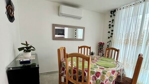 A dining area with a round table, wooden chairs, a black side table, a wall-mounted air conditioner, a mirror, and a window with curtains. - Peaceful 2-bedroom house with AC in charming Santa Marta, WIFI, Tayrona. (Santa Marta)