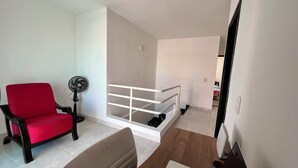 A living room with a red chair, a laptop on a wooden table, a white railing, and a fan. - Peaceful 2-bedroom house with AC in charming Santa Marta, WIFI, Tayrona. (Santa Marta)