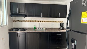 A kitchen with black cabinets, a stainless steel refrigerator, a gas stove, and a coffee maker. - Peaceful 2-bedroom house with AC in charming Santa Marta, WIFI, Tayrona. (Santa Marta)