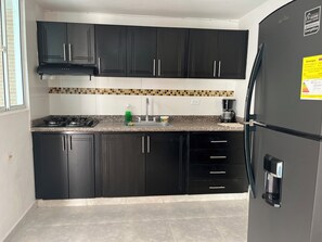 Una cocina con armarios negros, un refrigerador de acero inoxidable, una estufa a gas y una cafetera.