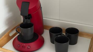 Une machine à café Senseo rouge avec quatre tasses noires posées sur un plateau.