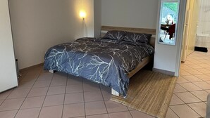 Un dormitorio con una cama, una lámpara en la pared, un espejo y una puerta que da a un baño.