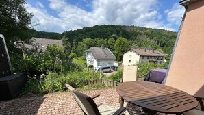 Un patio con una mesa y sillas, piso de ladrillo y vistas a casas y árboles al fondo.