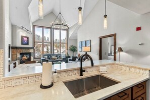 A modern kitchen with a large island, a fireplace, and a dining area with a sofa. - Remodeled Condo, Ski in/out with Hot Tub, Spa, Gym (Breckenridge)