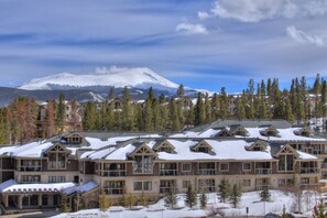 A large lodge with multiple buildings, snow-covered roofs, and a backdrop of mountains and trees. - Remodeled Condo, Ski in/out with Hot Tub, Spa, Gym (Breckenridge)