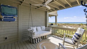 A wooden deck with a white swing chair, a white cushioned swing, and a ceiling fan. - Seaside Hideaway - Beach Front Luxury! (Johns Island)