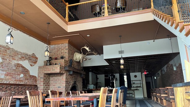 Un restaurante con paredes de ladrillo, mesas y sillas de madera, un balcón con barandillas de metal y faroles colgantes.