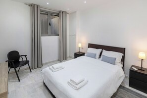 A hotel room with a bed, two bedside tables, a chair, a desk, and a window with curtains. - BES 1 - Spacious Modern 2-bed Apt by GHH (Kesariani)