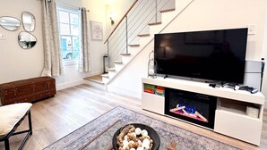 Moderni olohuone, jossa on portaikko, litteänäyttöinen televisio, takka ja maalaishenkinen pöytä, jonka päällä on kananmunia.