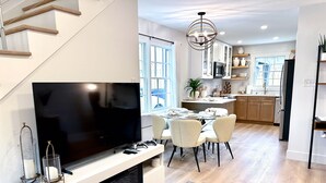 Moderni olohuone, jossa on litteänäyttöinen televisio, takka, ruokailutila, keittiö ja portaat.