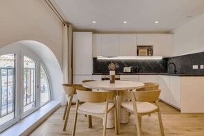A modern kitchen with a round dining table, wooden chairs, and a view through large windows. - A Cosy 2-Br/2BA Duplex - Louvre/Rivoli (Paris)